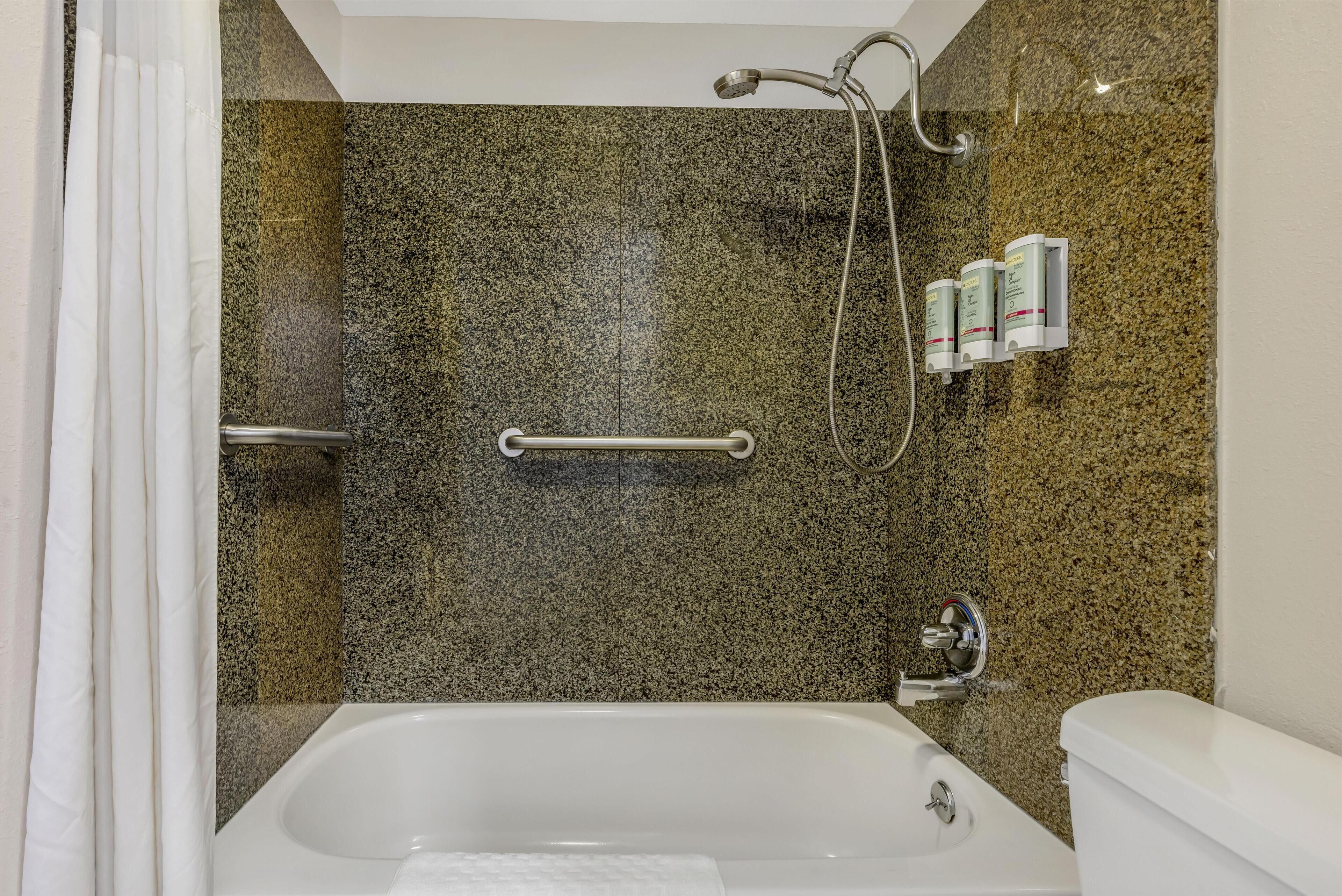 A bathroom with a granite shower wall, a white bathtub, and a toilet.