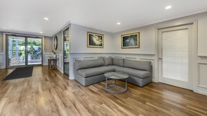 Een ruime woonkamer met een grijze modulaire bank, een glazen salontafel en een zwart vloerkleed.