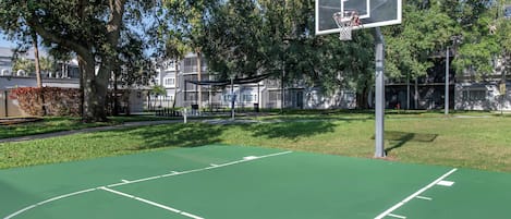 Een basketbalveld buiten, met een basketje, omringd door bomen en gebouwen.
