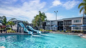 A swimming pool with two slides, surrounded by modern buildings and palm trees. - Orbit One Vacation Villas by Coolvacay (Kissimmee)