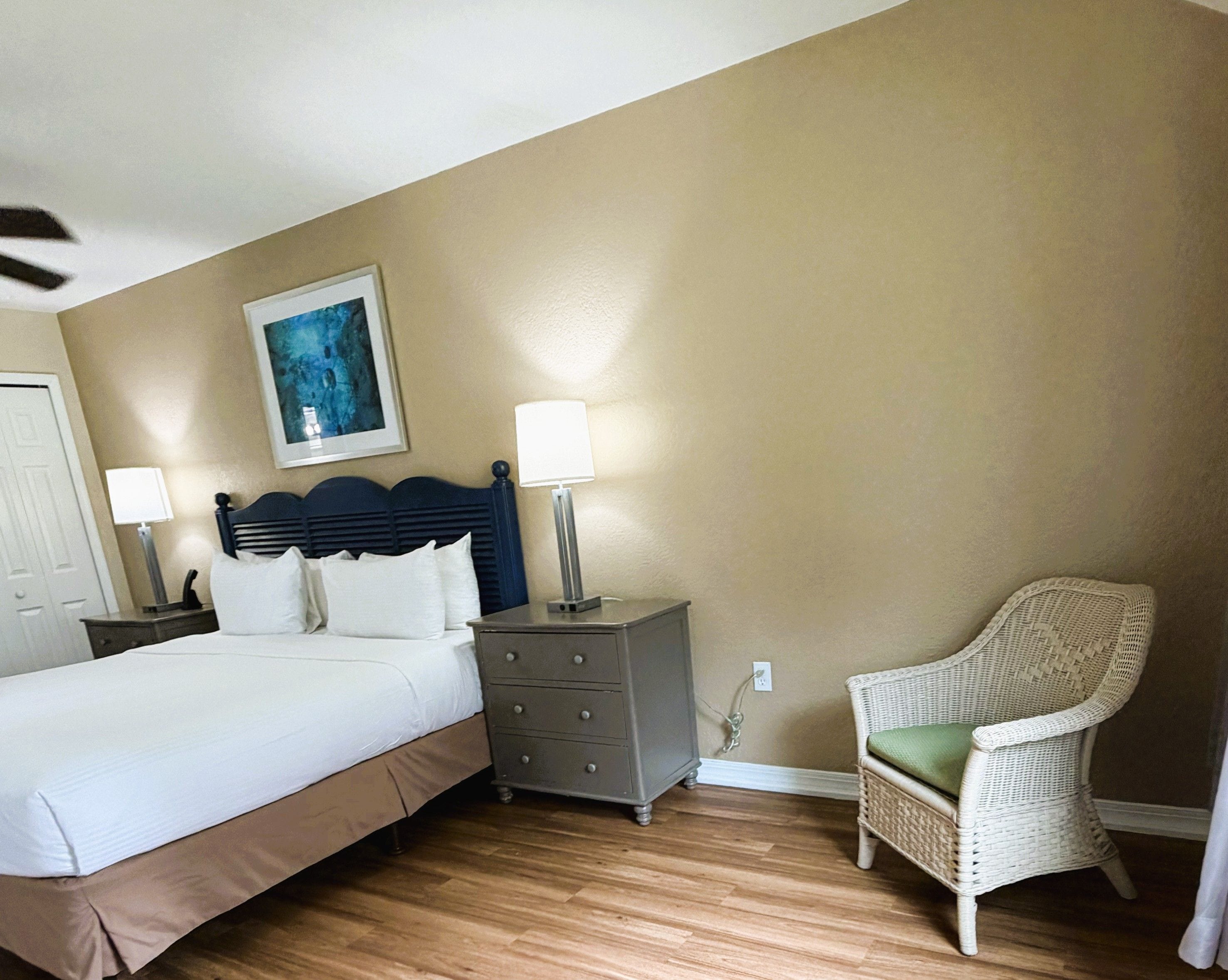 A bedroom with a bed, a dresser, two bedside lamps, a chair, and a painting on the wall.