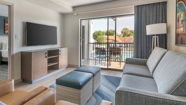 A modern hotel room with a large flat-screen TV, a grey sofa, a wooden cabinet, and a balcony with a pool view. - Orbit One Vacation Villas by Coolvacay (Kissimmee)