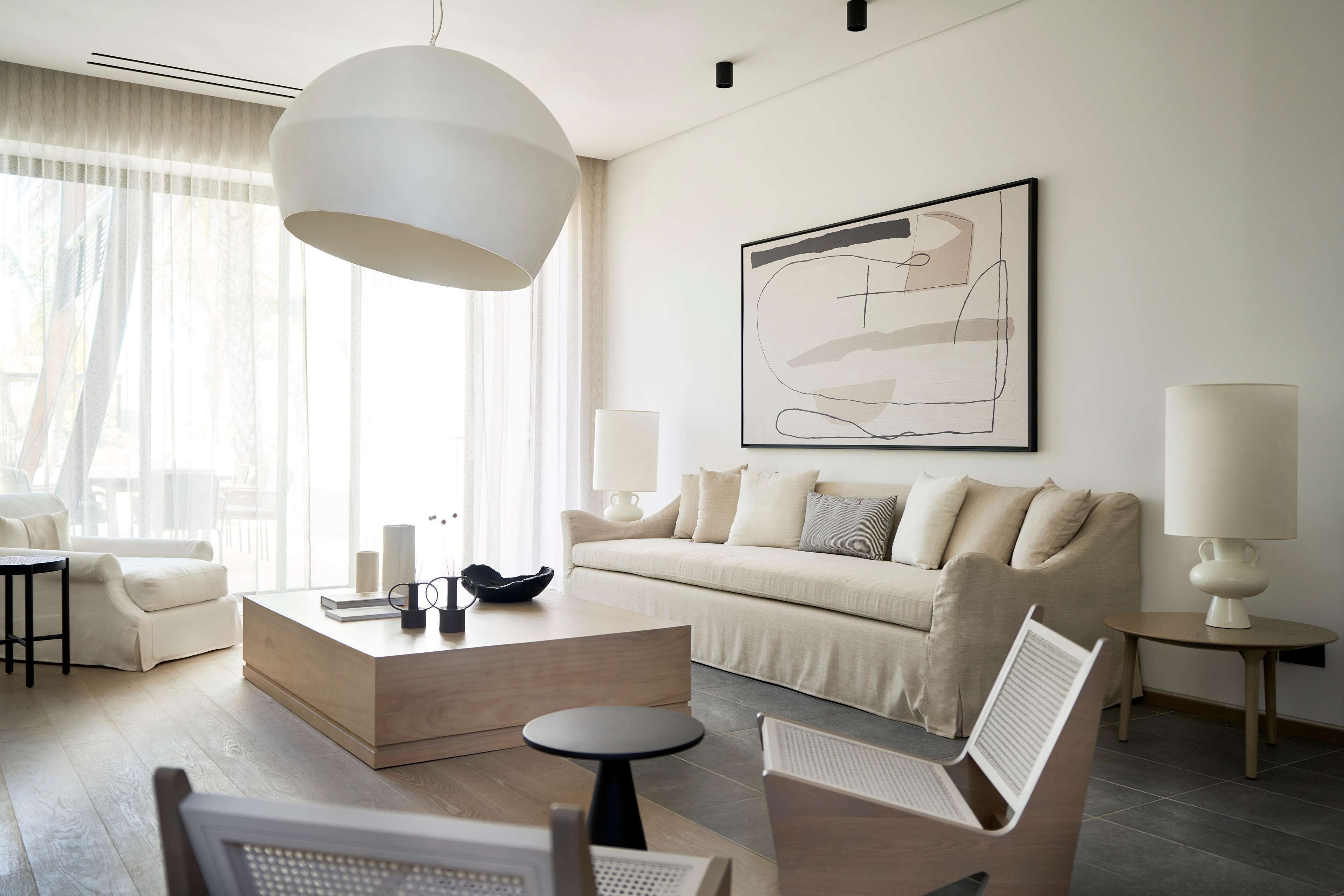 A modern living room with a sofa, coffee table, and chairs, a large abstract painting on the wall, and a large pendant light.