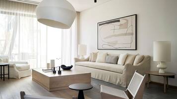 A modern living room with a sofa, coffee table, and chairs, a large abstract painting on the wall, and a large pendant light.