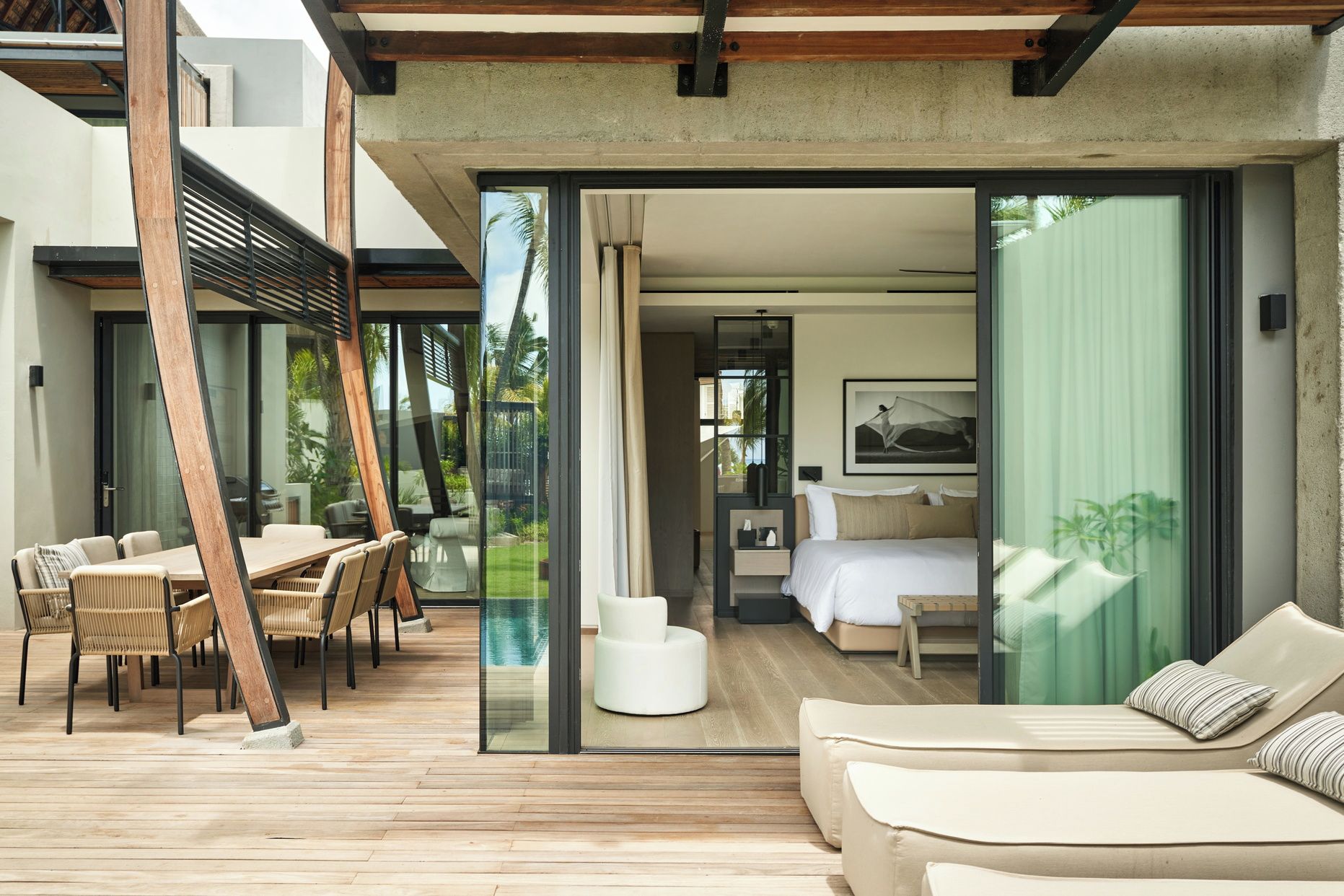 Habitación de hotel moderna con puerta de vidrio que da a un área de piscina, cama con un ventanal grande y zona de comedor con mesa y sillas.