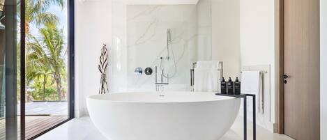 A modern bathroom with a freestanding bathtub, a glass shower enclosure, and a view of palm trees.