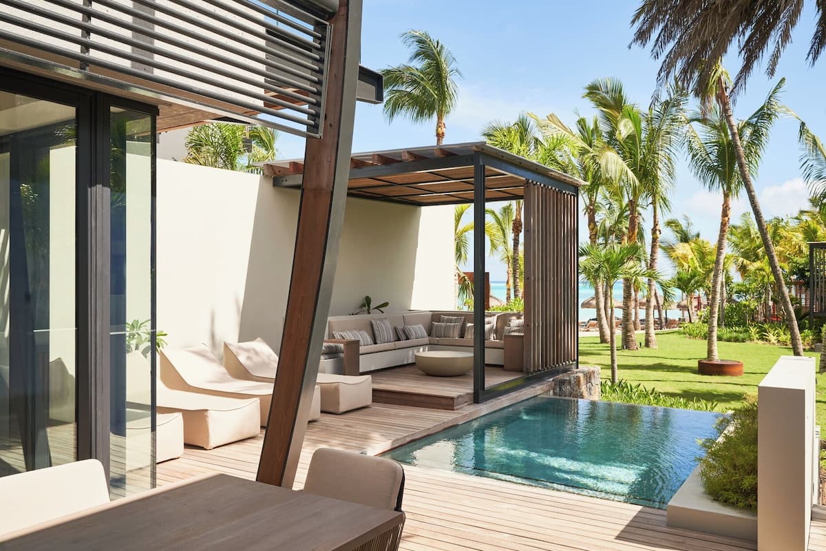 Een modern buitenzwembad met een houten terras, een overdekte zitplaats en uitzicht op de oceaan.