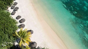 An aerial view of a beach with clear turquoise water, white sand, and several thatched umbrellas.