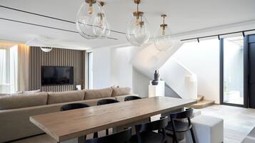 Una sala de estar moderna con una mesa de comedor de madera, sillas negras, un sofá beige y un televisor montado en la pared.