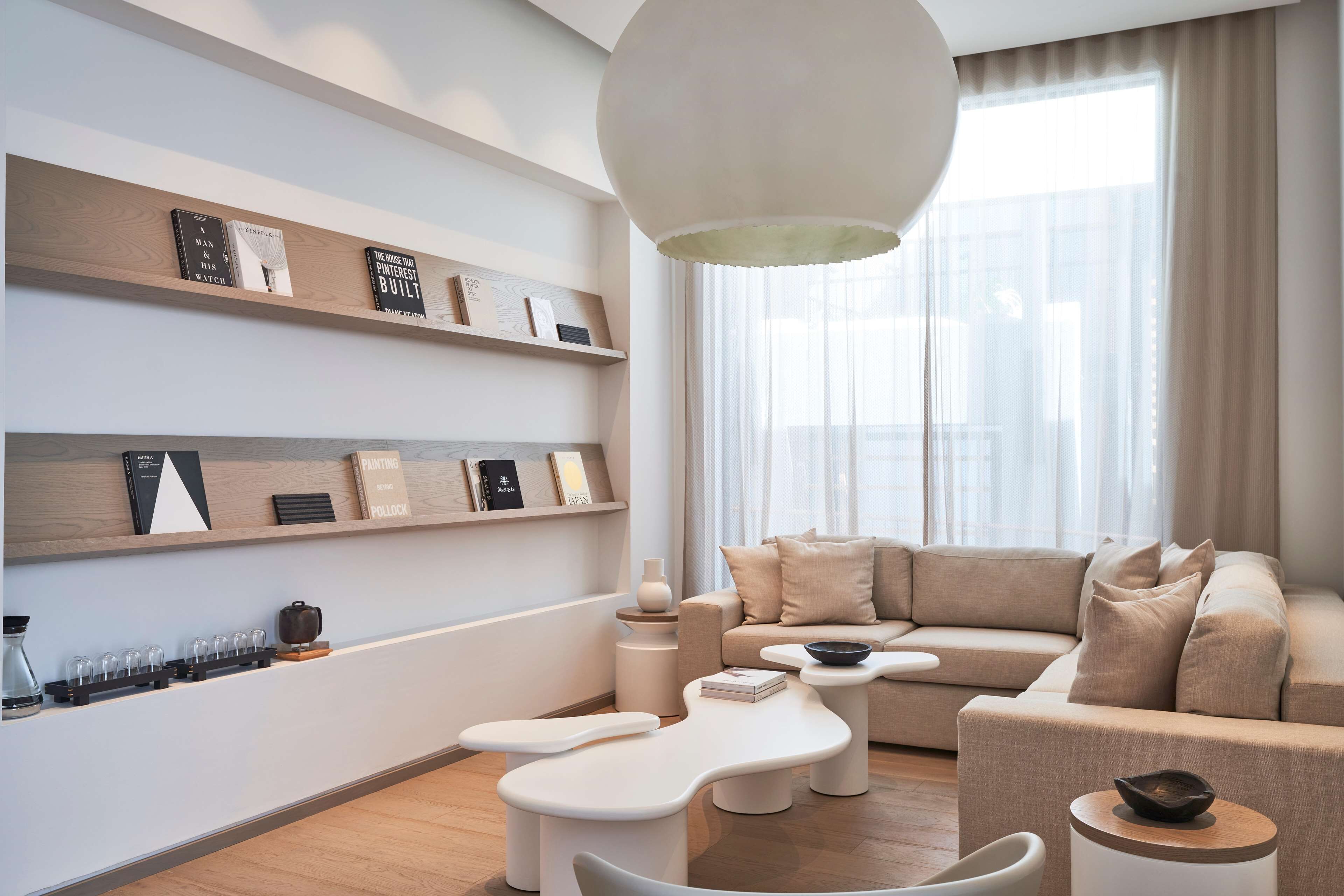 Una sala de estar moderna con un sofá, una mesa de centro y una mesita auxiliar. Se observan estanterías con libros y objetos decorativos.