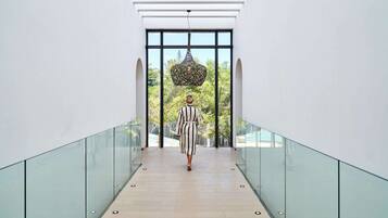 Un interior moderno con barandilla de cristal, una persona caminando por un pasillo y vistas de vegetación al exterior.