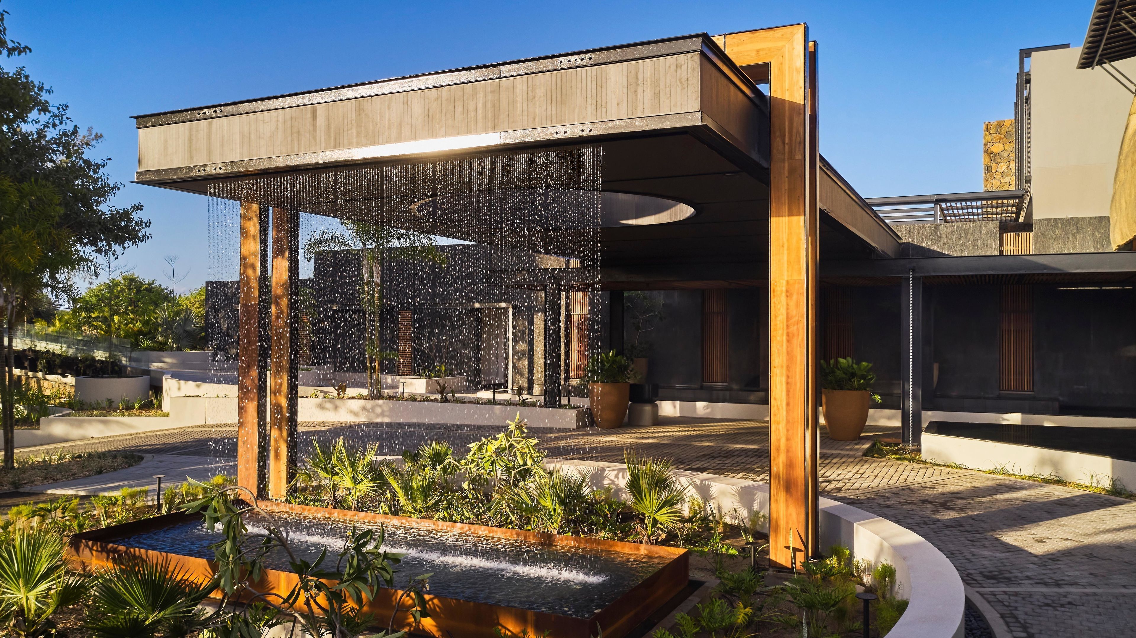 A modern building with a water feature, outdoor seating, and potted plants.