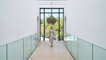 Un interior moderno con barandilla de vidrio, una persona caminando por un pasillo y vistas de la vegetación al exterior.