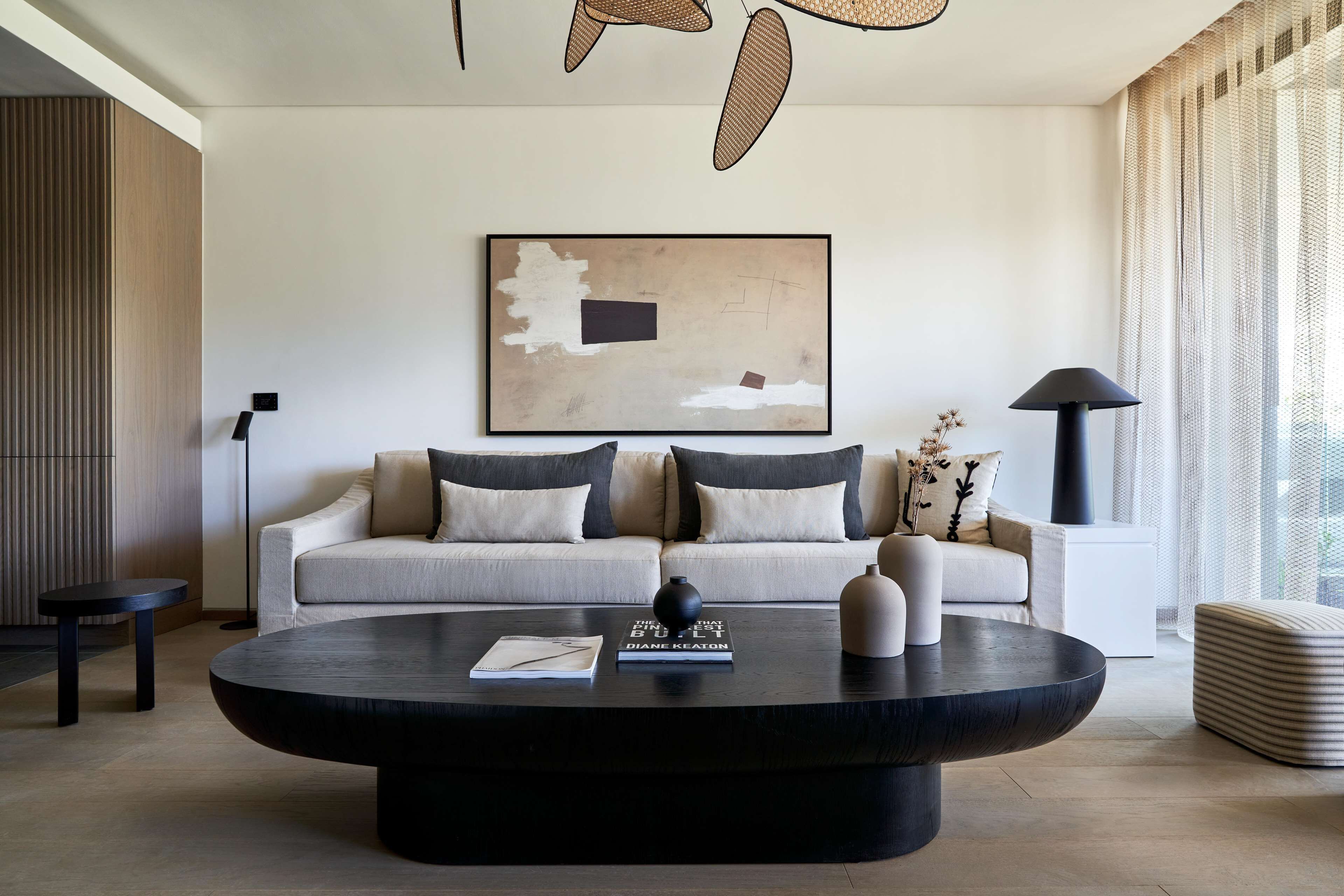 Ein modernes Wohnzimmer mit rundem Couchtisch, einer Sofaecke mit Kissen sowie einem gerahmten abstrakten Gemälde und einer Stehlampe.