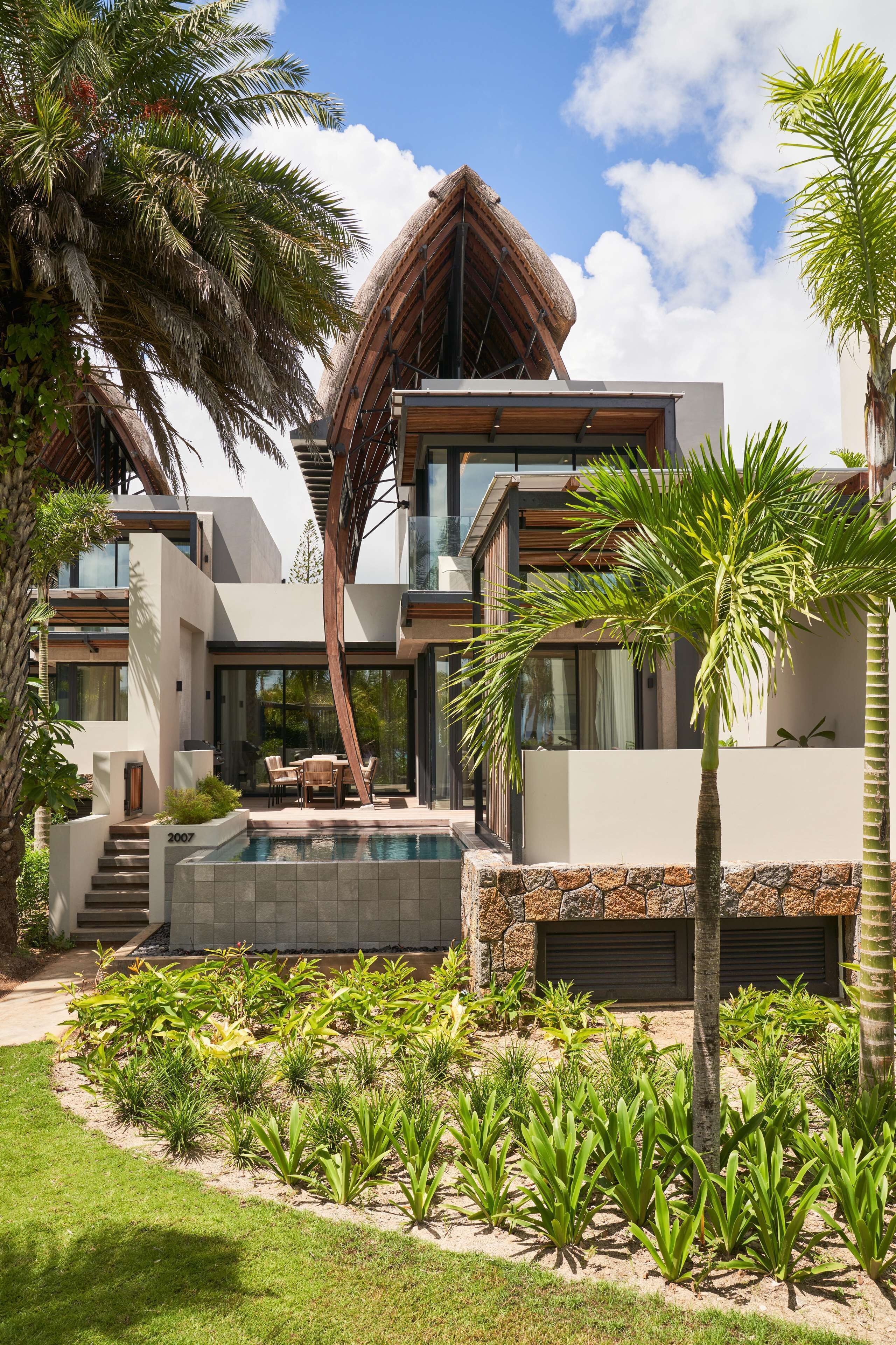 Una casa moderna con piscina, palmeras y un muro de piedra.