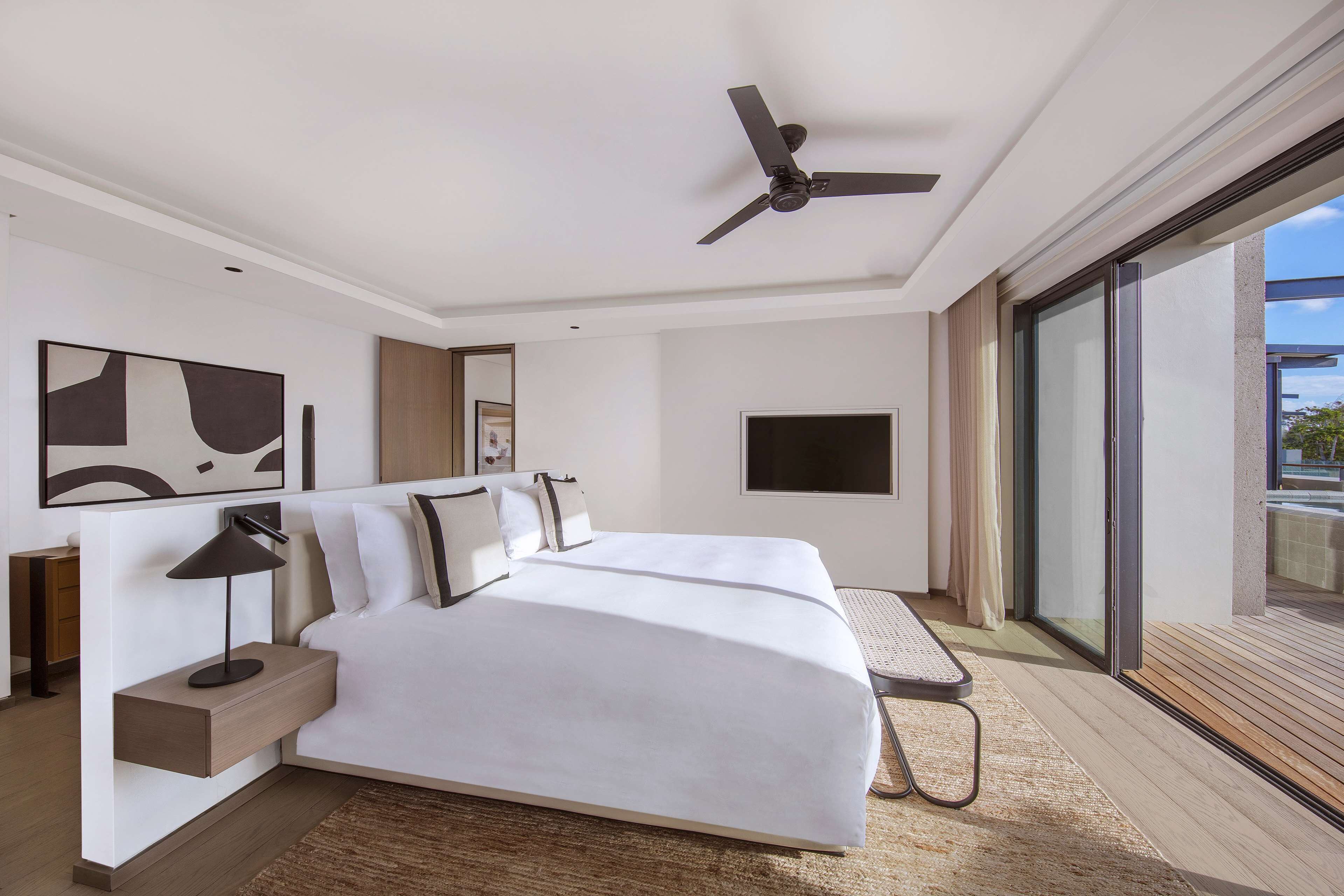 A modern hotel room with a large bed, a ceiling fan, a flat-screen TV, and a balcony with a view.