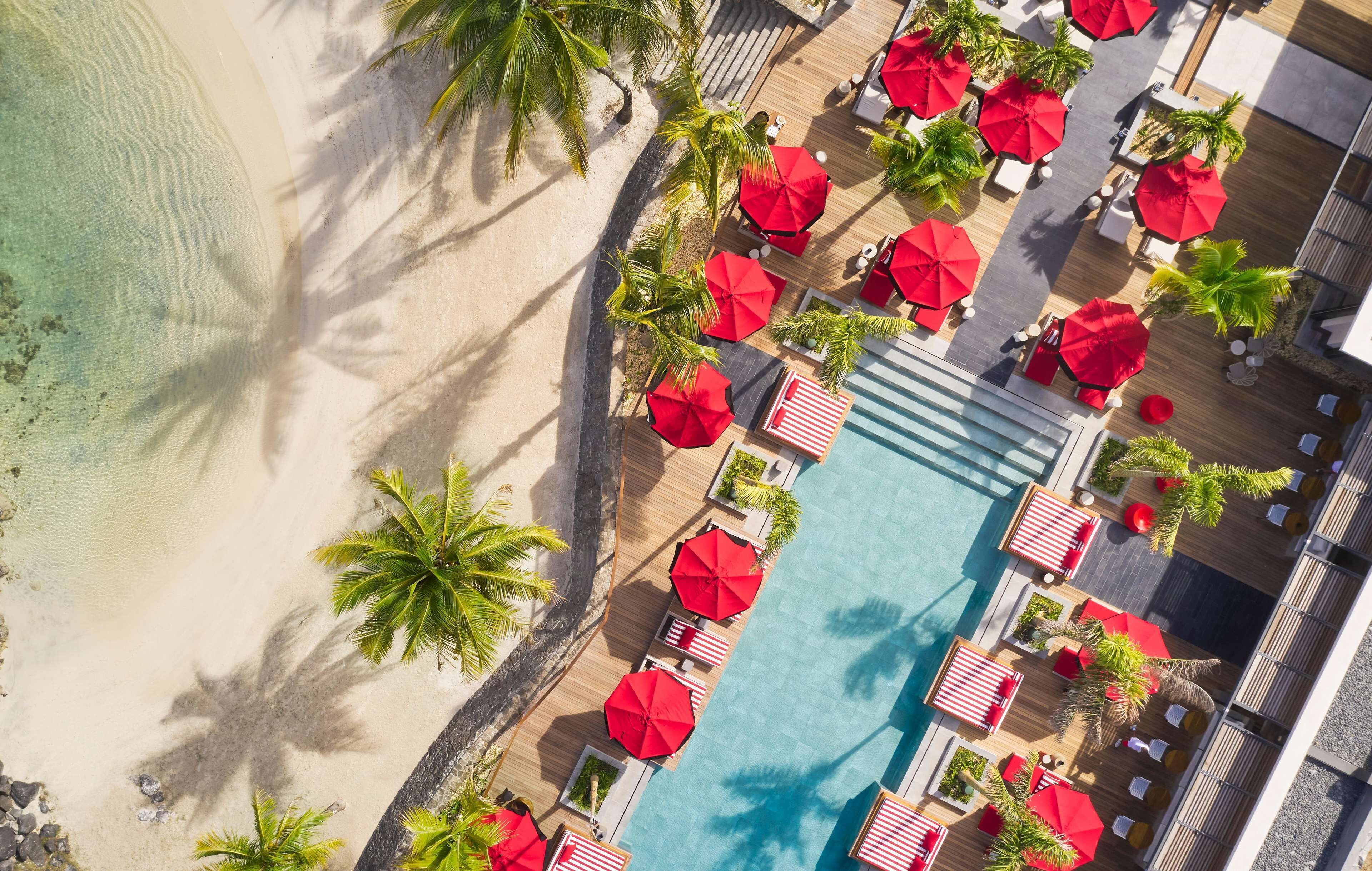 Vista aérea de un resort con piscina, sombrillas rojas y palmeras.