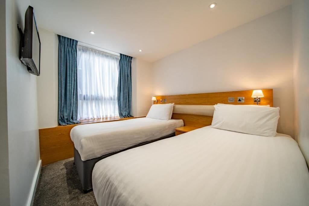 A hotel room with two beds, a TV, and a window with curtains.