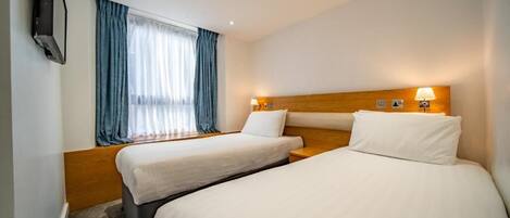 A hotel room with two beds, a TV, and a window with curtains.