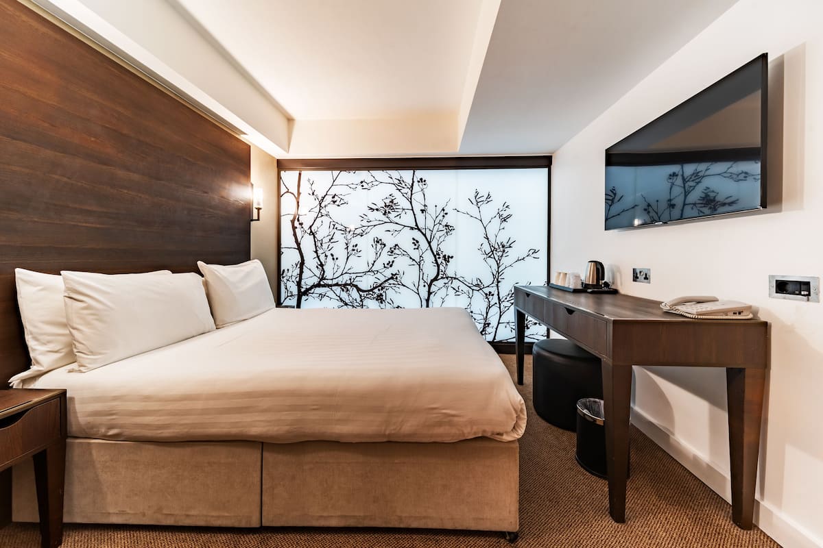 A modern hotel room with a large bed, a desk, and a view of bare trees through a window.