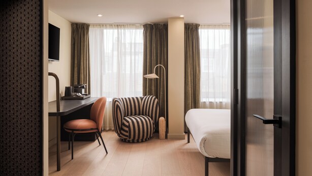 A hotel room with a bed, a desk with a chair, a television, and a lamp. - Central Park Hotel (London)