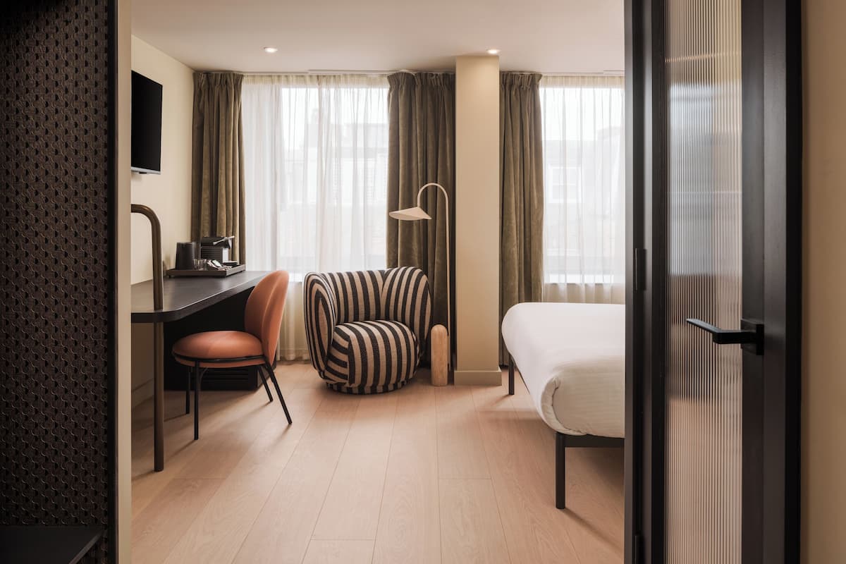 A hotel room with a bed, a desk with a chair, a television, and a lamp.
