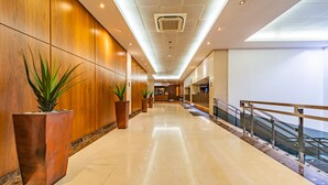 A modern hotel corridor with wooden panel walls, large potted plants, a marble floor, and a glass railing. - Central Park Hotel (London)