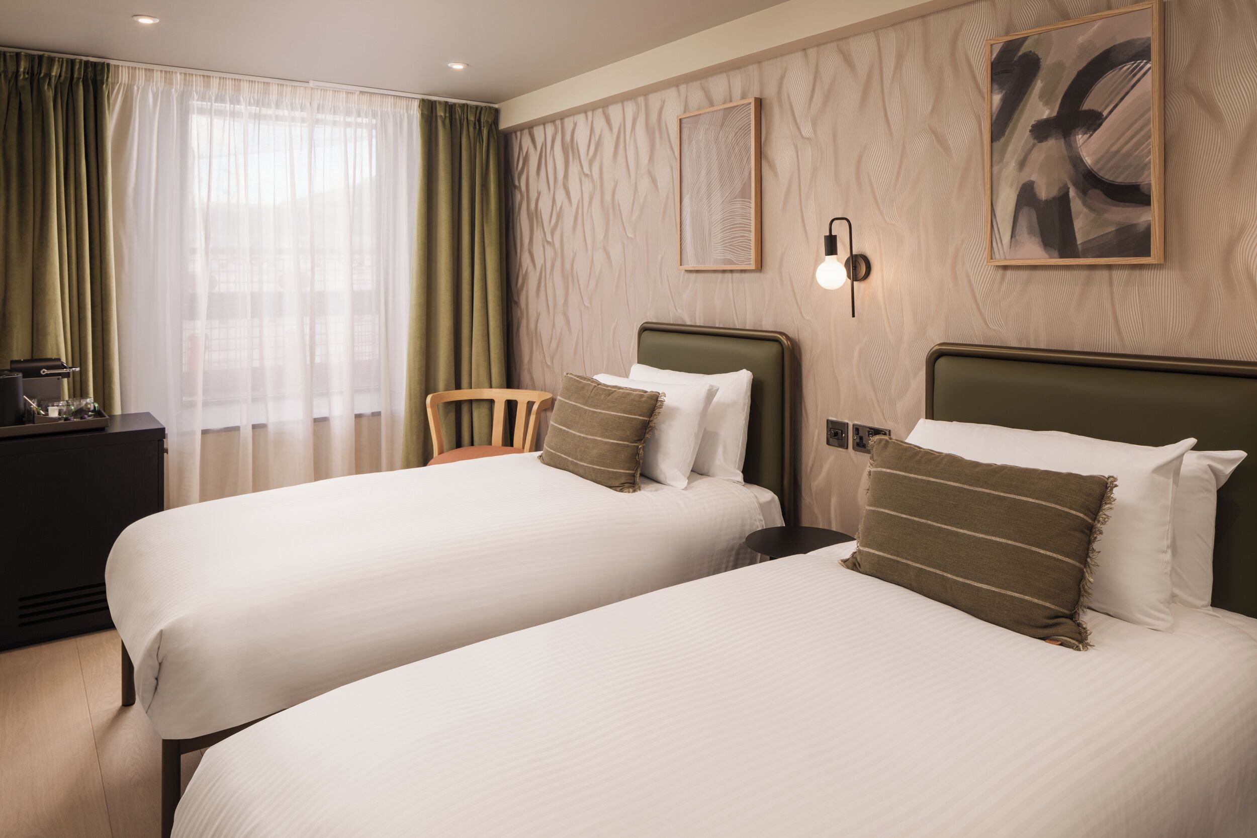A hotel room with two beds, a desk, and a chair.
