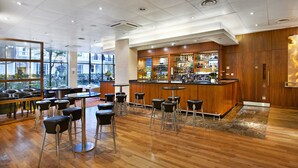 A bar area with wooden paneling, a counter with various bottles, and several black bar stools. - Central Park Hotel (London)