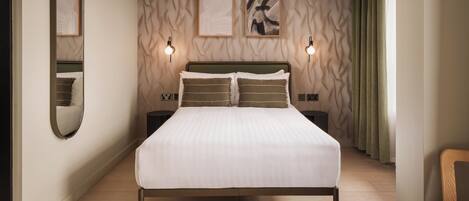 A modern bedroom with a large bed, two bedside tables, a mirror, and abstract wall art.