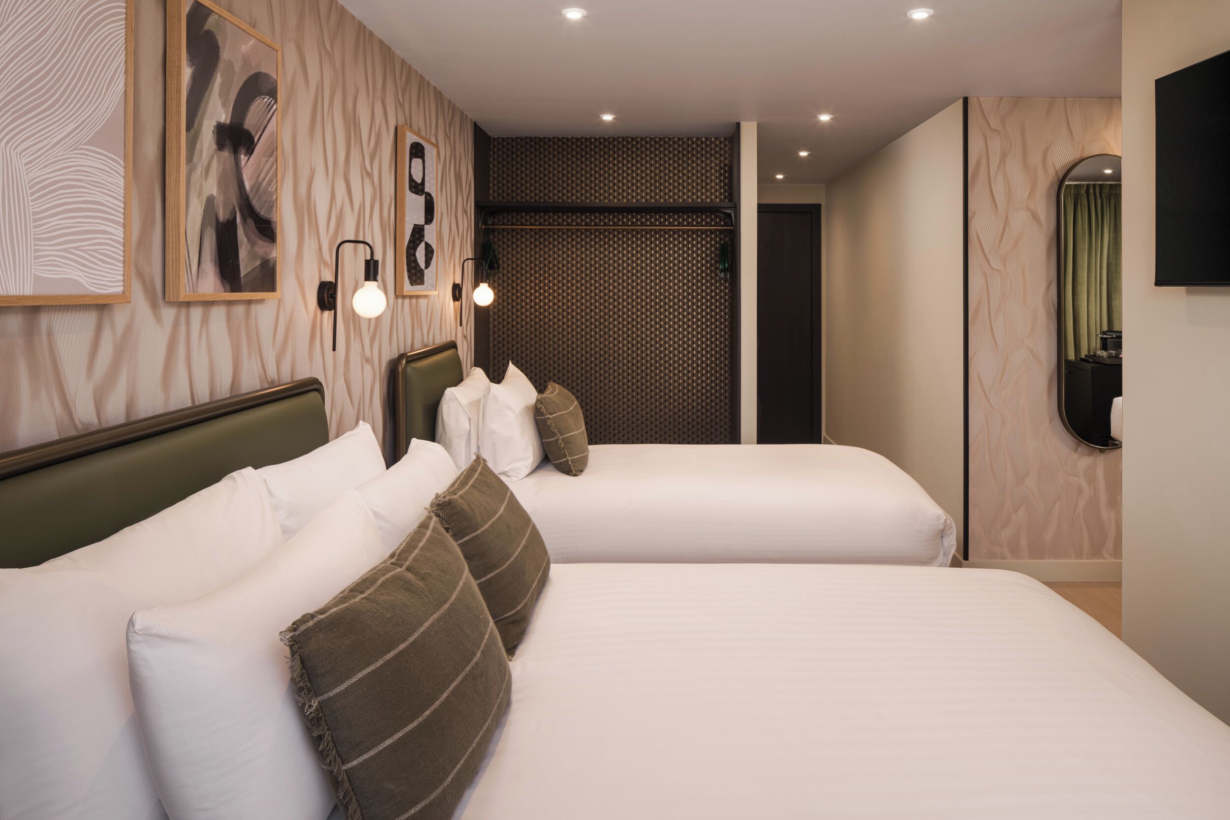 A hotel room with two beds, a large mirror, and wall-mounted artwork.