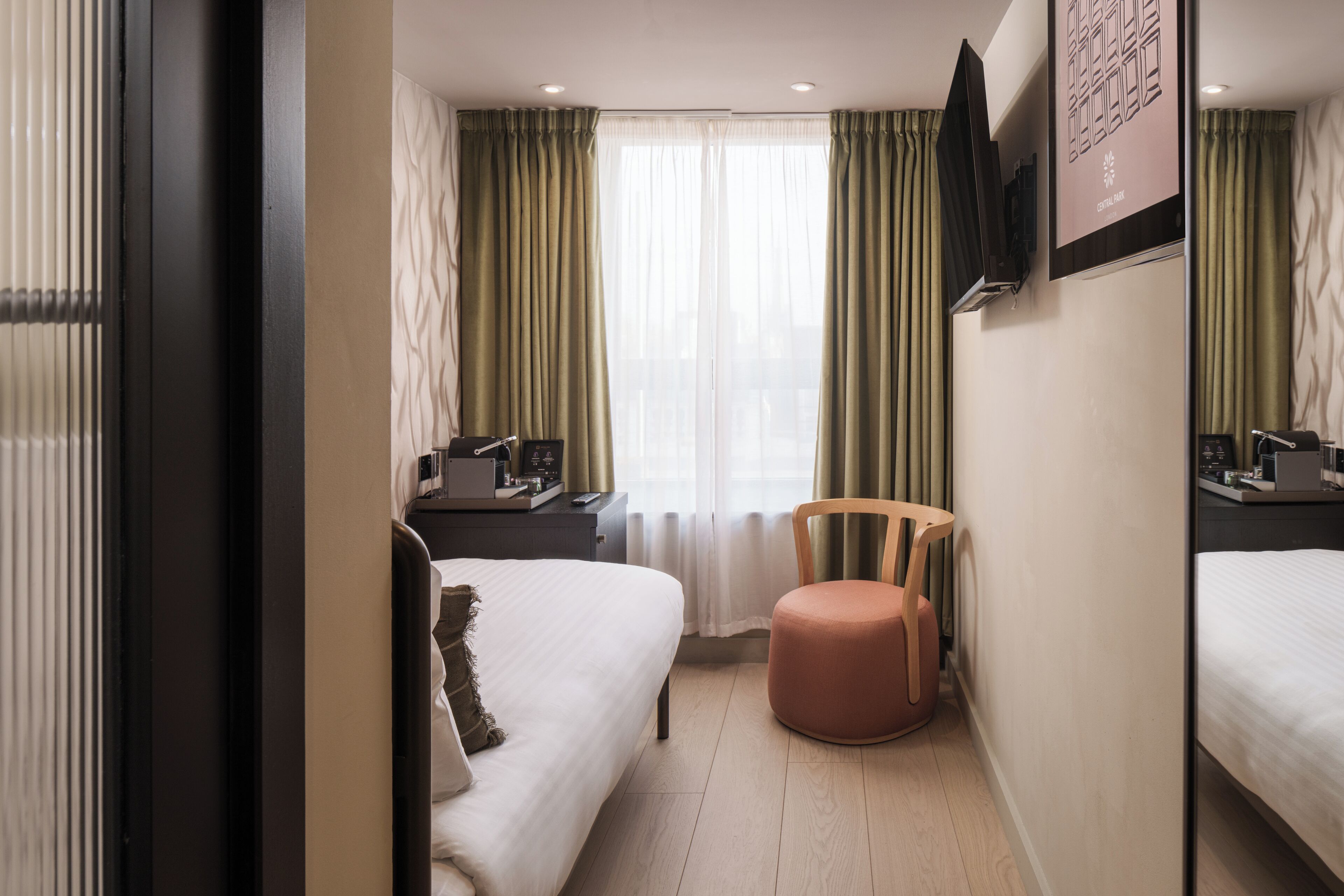 Une chambre d’hôtel avec un lit, une chaise, un bureau et un téléviseur fixé au mur.