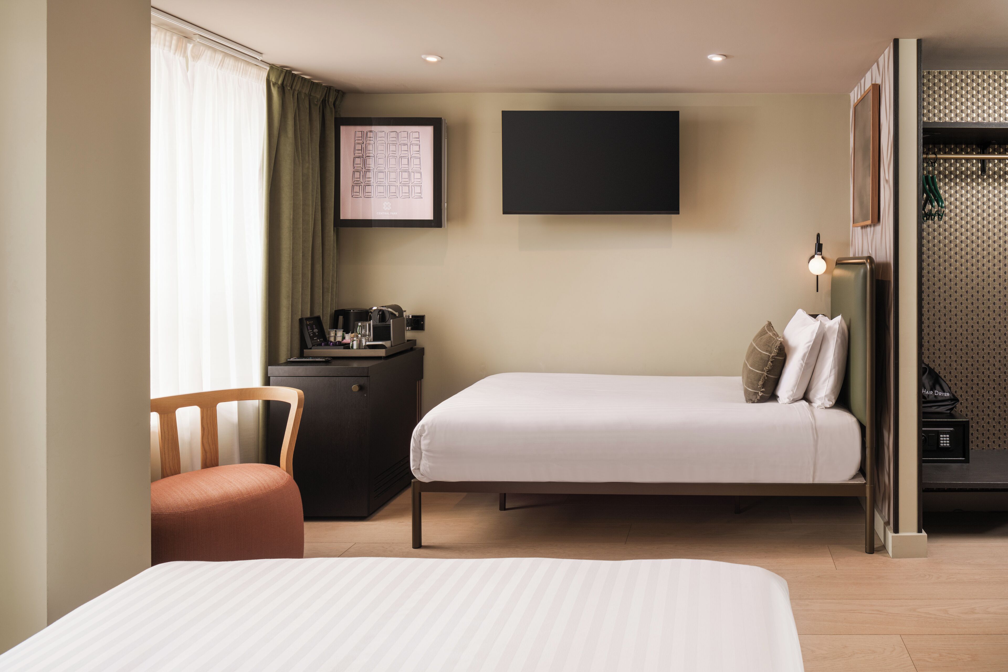 A hotel room with two beds, a desk, a chair, a TV, and a wardrobe.