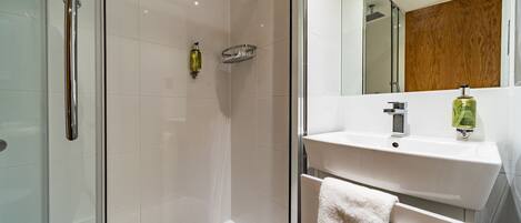 A modern bathroom with a glass shower enclosure, a white sink, and a wooden panel wall.