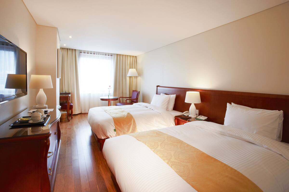 Una habitació d'hotel amb dos llits, un televisor, una escriptori amb una làmpada i una cadira.
