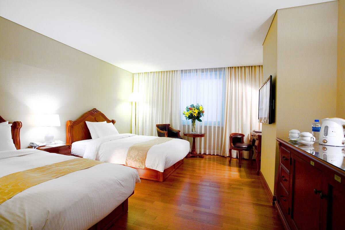 Habitació d'hotel amb dos llits, un escriptori amb cadira, una taula petita amb un ram de flors i una cafetera.