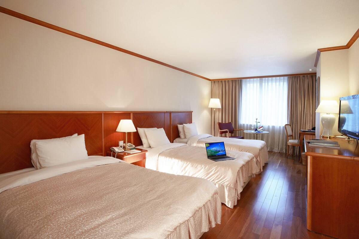 Habitació d'hotel amb dos llits, una escriptori amb un ordinador portàtil, una televisió i una cadira.