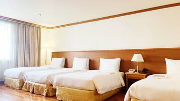 A hotel room with three beds, wooden headboards, and a large window with curtains.