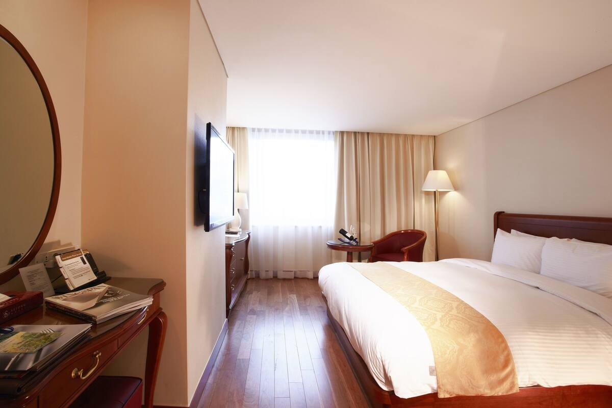 Habitació d'hotel amb un llit gran, un escriptori amb una cadira, una làmpada i una finestra amb cortines.