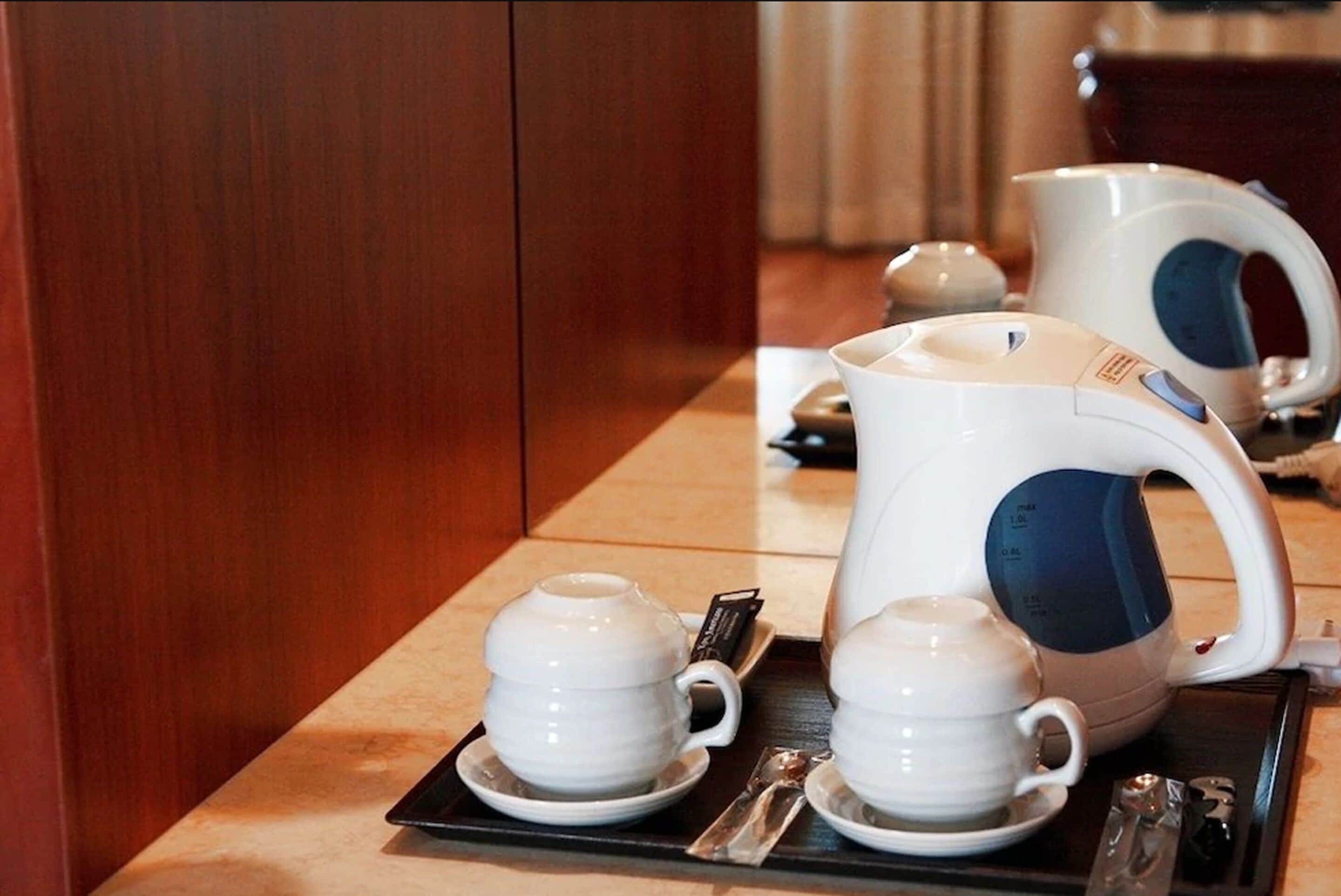 A hotel room with a wooden cabinet, a table with a tea set including a teapot, two cups, and a tray.