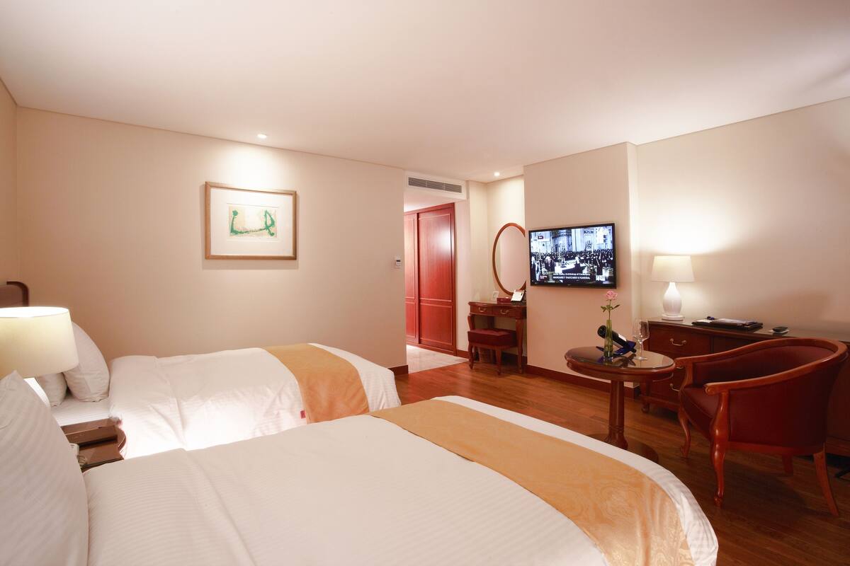 Una habitació d'hotel amb dos llits, una taula de treball, una cadira, un televisor i un quadre al mur.