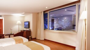 A hotel room with two beds, a desk, a TV, and a large window with a city view. - Sejong Hotel (Seoul)