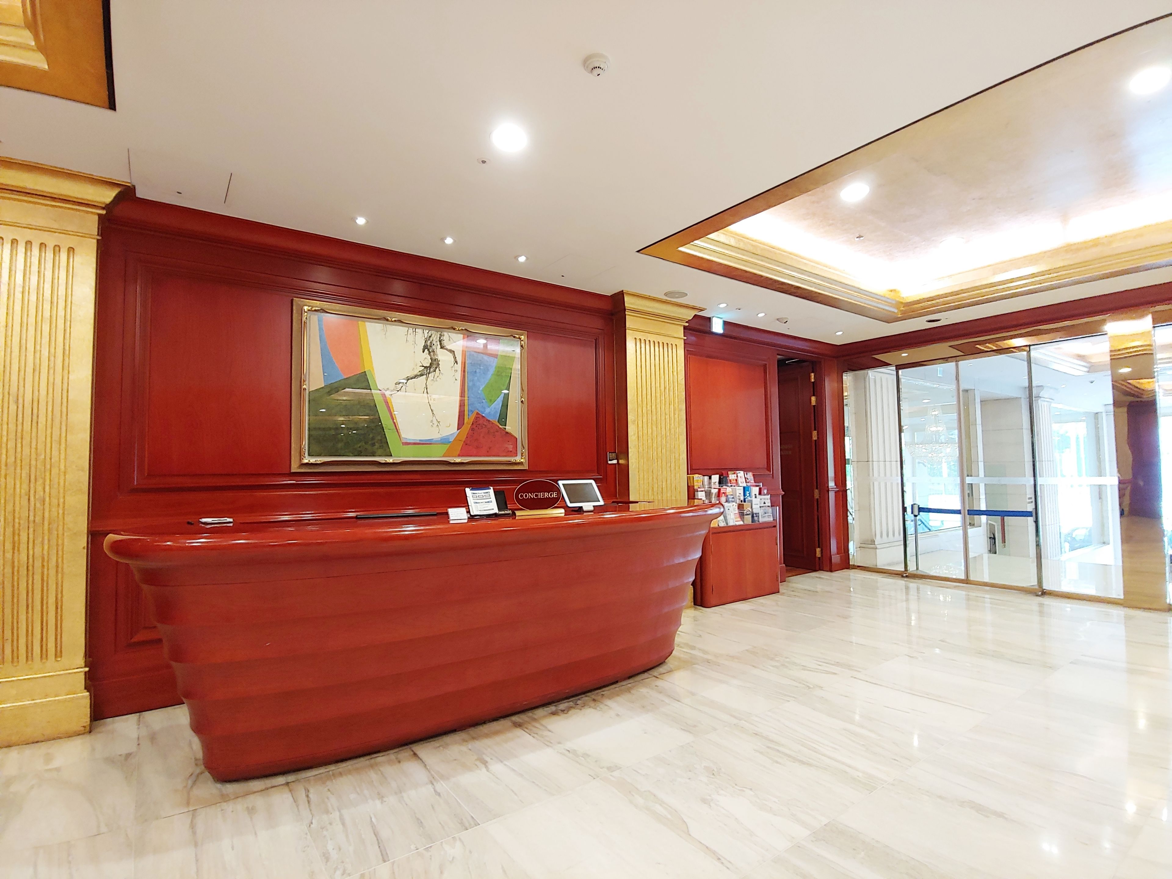 A reception area with a marble floor, a red reception desk, a large abstract painting, and a glass door leading to another room.