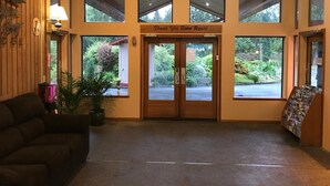 A reception area with a wooden wall, a couch, a potted plant, and a sign that reads "Thank You Come Again." - Sequim Bay Lodge (Sequim)