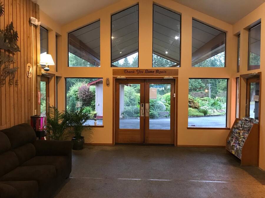 A reception area with a wooden wall, a couch, a potted plant, and a sign that reads "Thank You Come Again."