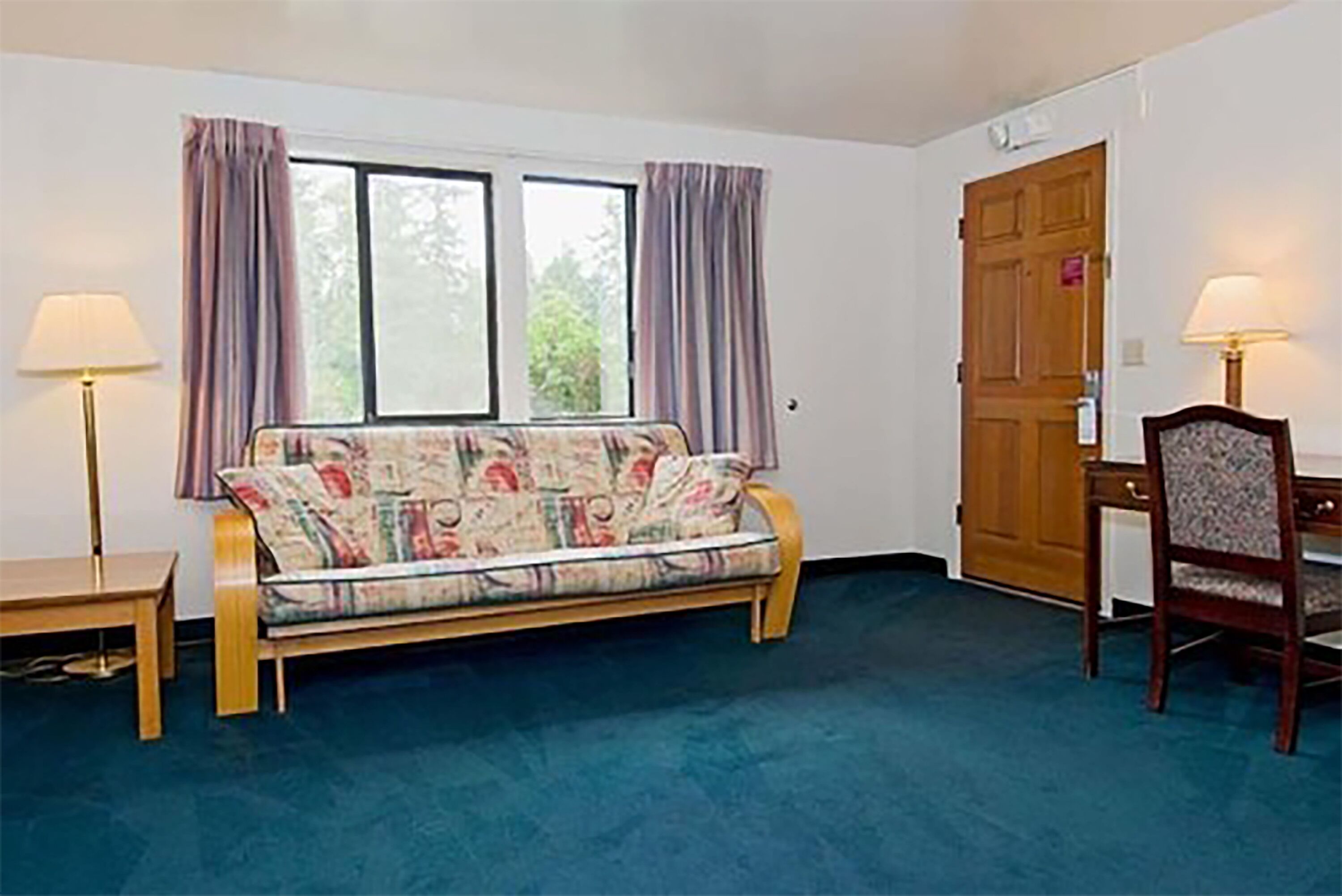 A room with a sofa, a chair, a desk, and a door.