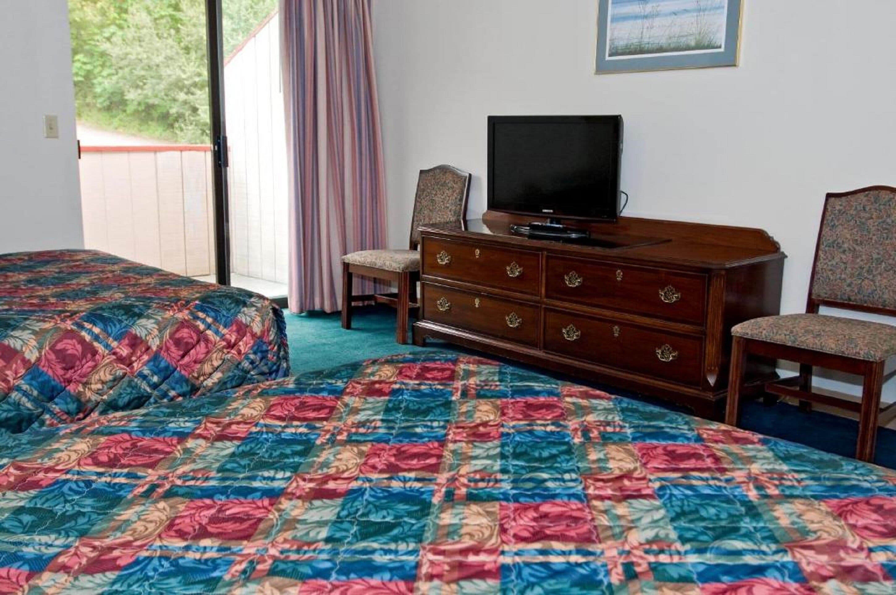 A bedroom with a large bed, a wooden dresser, a television, and a chair.
