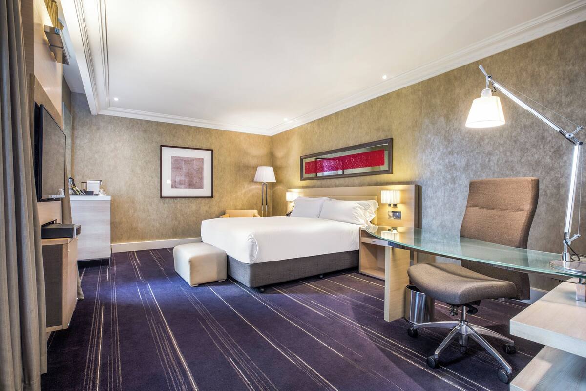 A hotel room with a bed, desk, chair, and a large mirror.