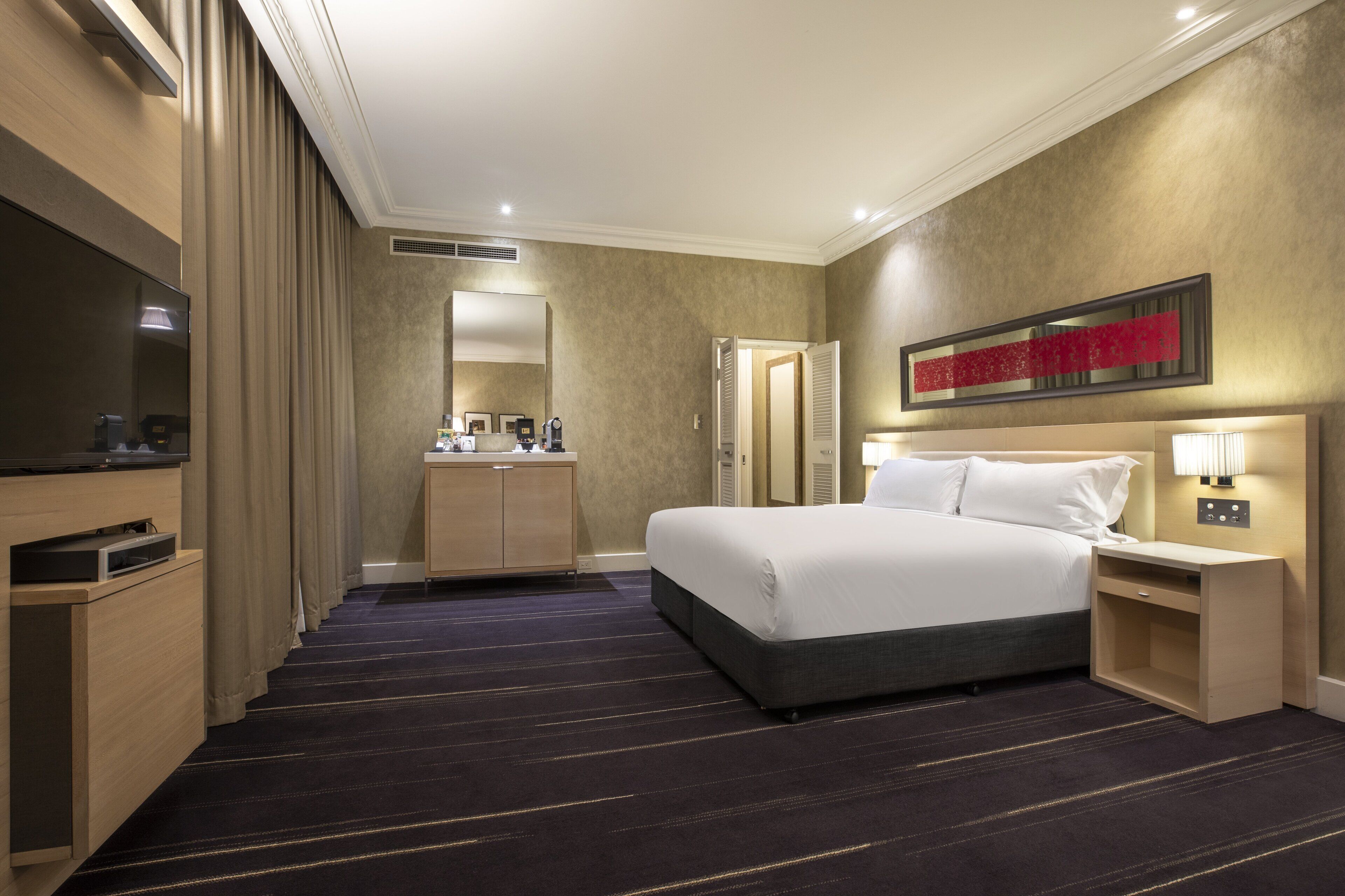 A hotel room with a large bed, a TV, a desk, and a mirror.