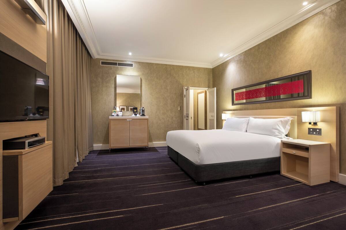 A hotel room with a large bed, a TV, a desk, and a mirror.